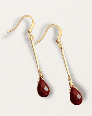 Gold earrings with red teardrop-shaped stones on a light gray background