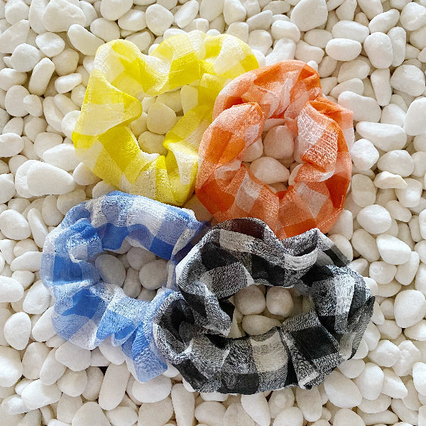 Four colorful scrunchies on a textured white surface