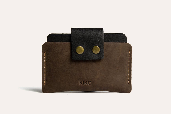 Brown leather wallet with black flap and gold buttons on a light gray background
