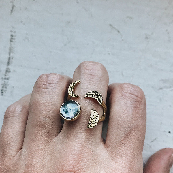 Gold ring with moon design on a finger against a neutral background