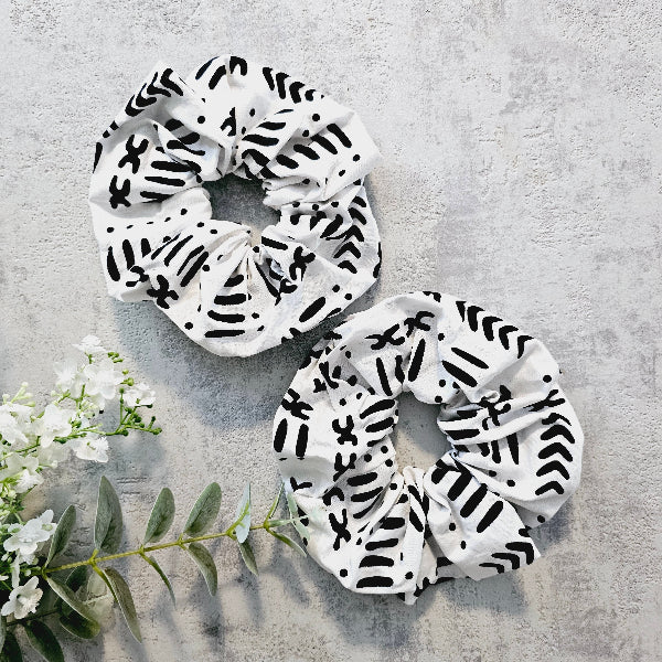 Two white scrunchies with black abstract patterns on a light gray background.