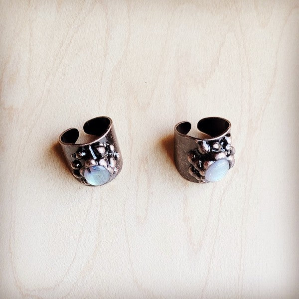 Pair of silver cuff earrings with gemstones on a beige background