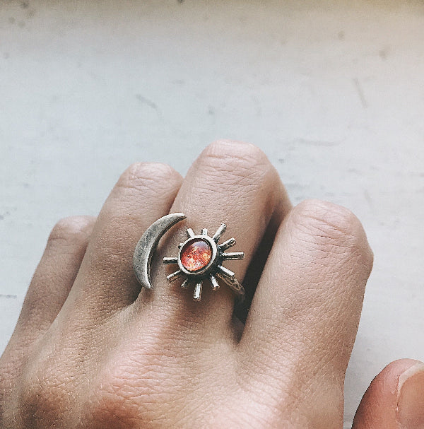 Silver ring with sun and moon design on a finger against a neutral background