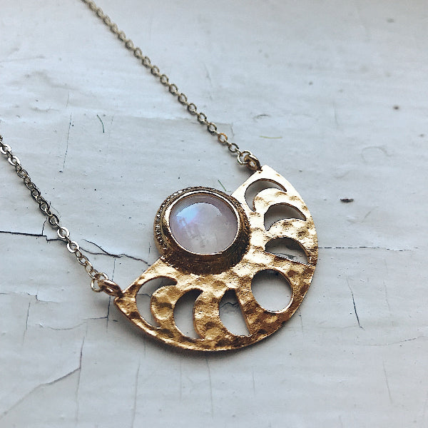 Gold pendant necklace with a central gemstone on a textured white background