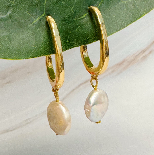 Gold hoop earrings with pearl drops on a green leaf background