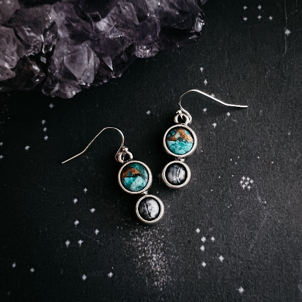 Pair of earrings with circular designs on a dark surface with crystals.