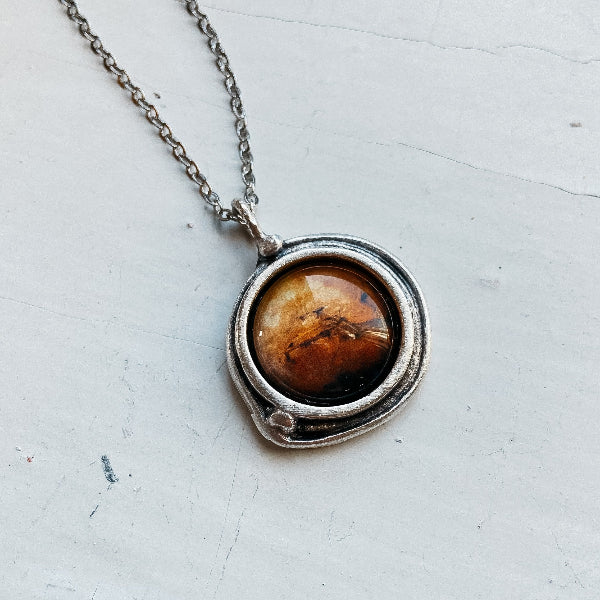 Necklace with a round pendant featuring a brown stone on a white surface