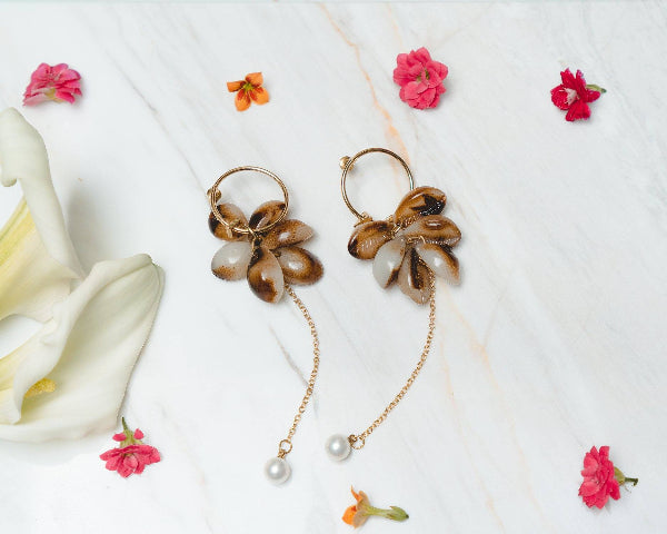 Pair of floral earrings with pearl accents on a white background with flowers.