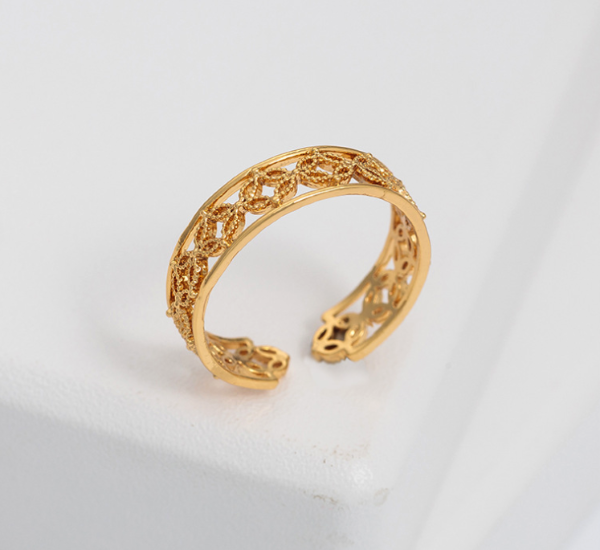 Gold open ring with intricate design on a light gray background