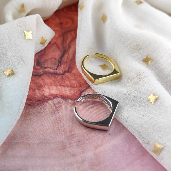 Two rings, one gold and one silver, on a textured fabric background.