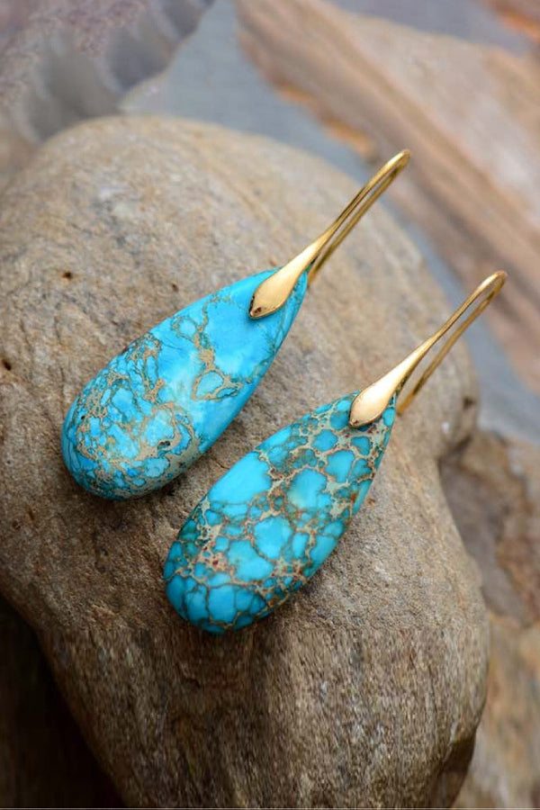 Turquoise earrings with gold hooks on a rock