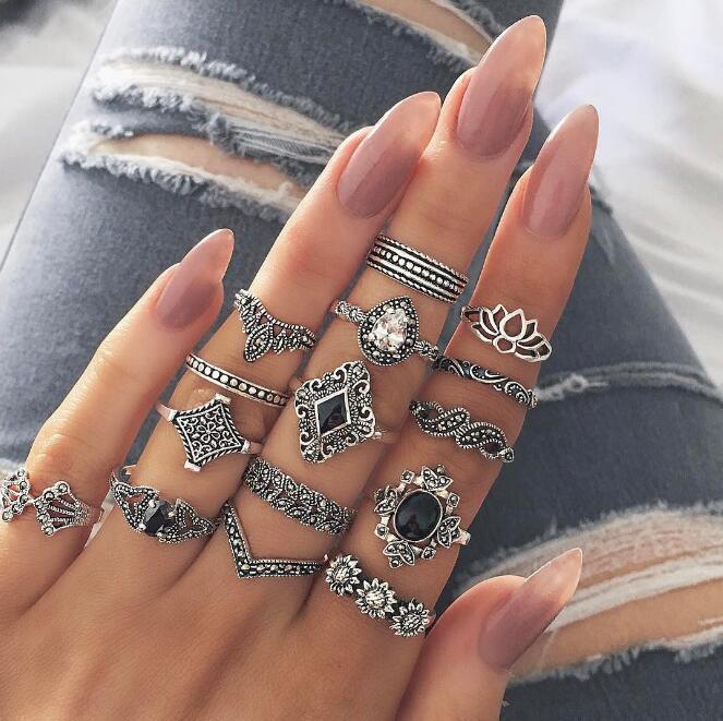 Hand wearing multiple silver rings with various designs on a blurred denim background