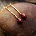 Gold earrings with red teardrop-shaped stones on a textured stone surface