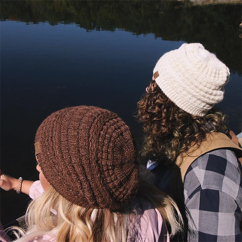 Two people wearing knit hats looking at a reflective body of water.