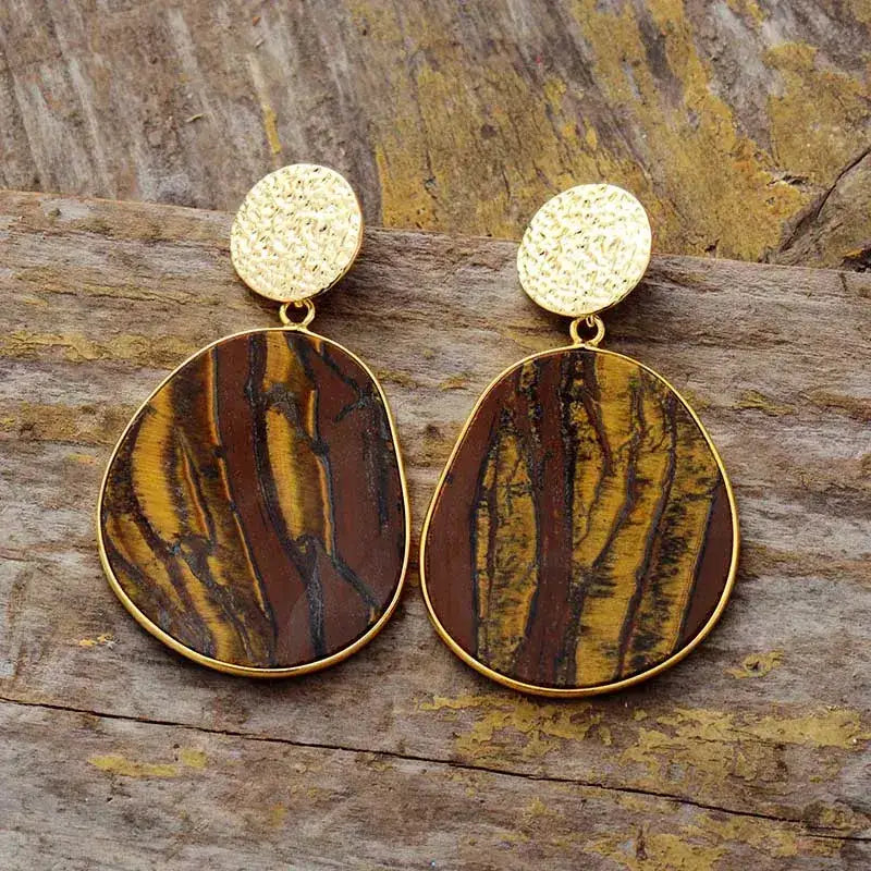 Gold and brown patterned earrings on a wooden surface