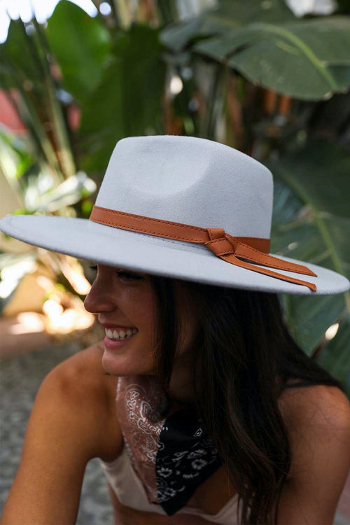 Woman wearing a wide-brimmed white hat with a brown band in a tropical setting