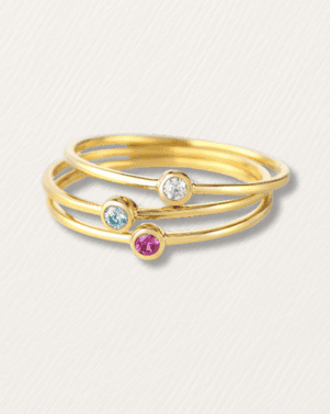 Set of three gold rings with embedded gemstones on a light gray background