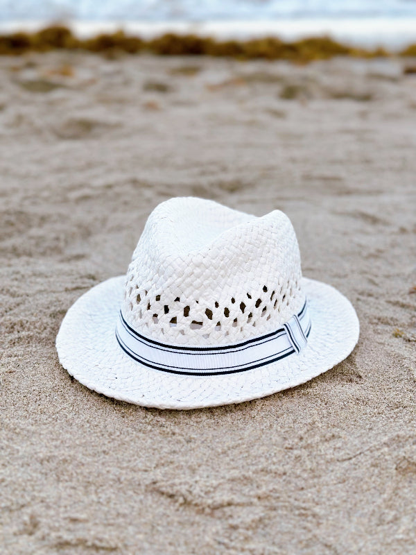 White straw hat with a black band on a sandy beach