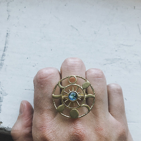Gold ring with a central blue gemstone on a hand against a light background