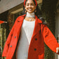 Woman wearing a red coat and beret standing outdoors.