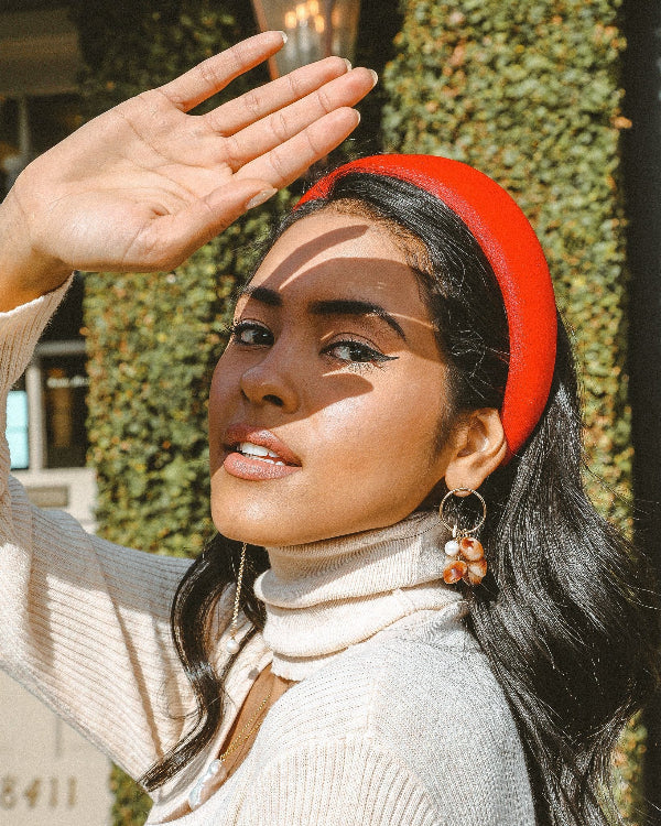 Woman wearing a red headband and beige turtleneck sweater outdoors.