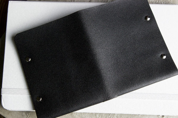 Black leather notebook with metal rings on a white surface