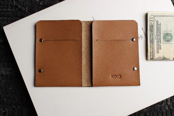 Brown leather wallet with 'Kiko' branding on a white surface with money.