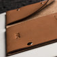 Close-up of a brown leather wallet with a brand logo on a light surface.