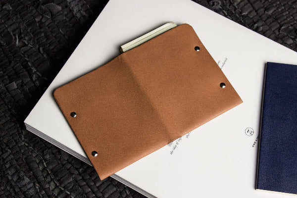 Brown leather notebook cover on a white book with a black textured background