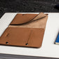 Brown leather clutch on a white surface with a blue notebook in the background
