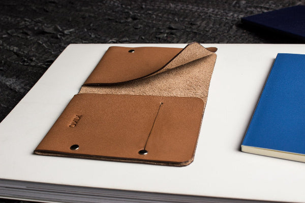 Brown leather clutch on a white surface with a blue notebook in the background