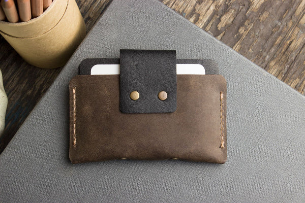 Brown leather wallet with black flap on a gray surface