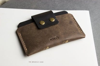 Brown leather wallet with black flap and gold buttons on a white surface