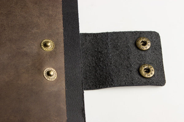 Close-up of brown leather and black fabric with gold buttons on a white background