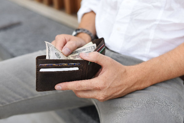 Person holding a wallet with money, sitting on a couch.