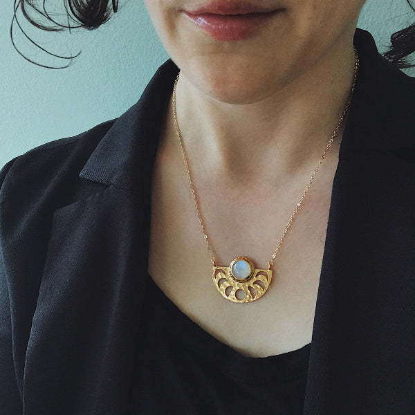 Person wearing a gold necklace with a circular pendant against a light blue background