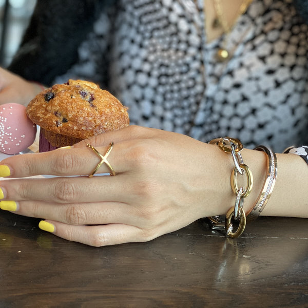 Hand with gold jewelry on a wooden surface with a muffin and pink candle in the background