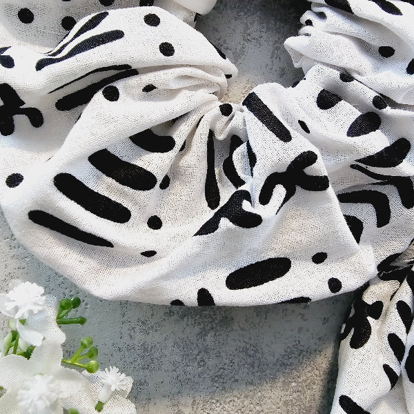 White scrunchies with black abstract patterns on a gray surface with white flowers.