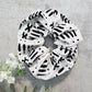 White scrunchie with black abstract patterns on a gray surface with white flowers.