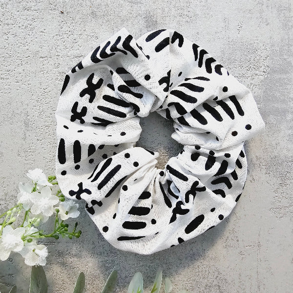 White scrunchie with black abstract patterns on a gray surface with white flowers.