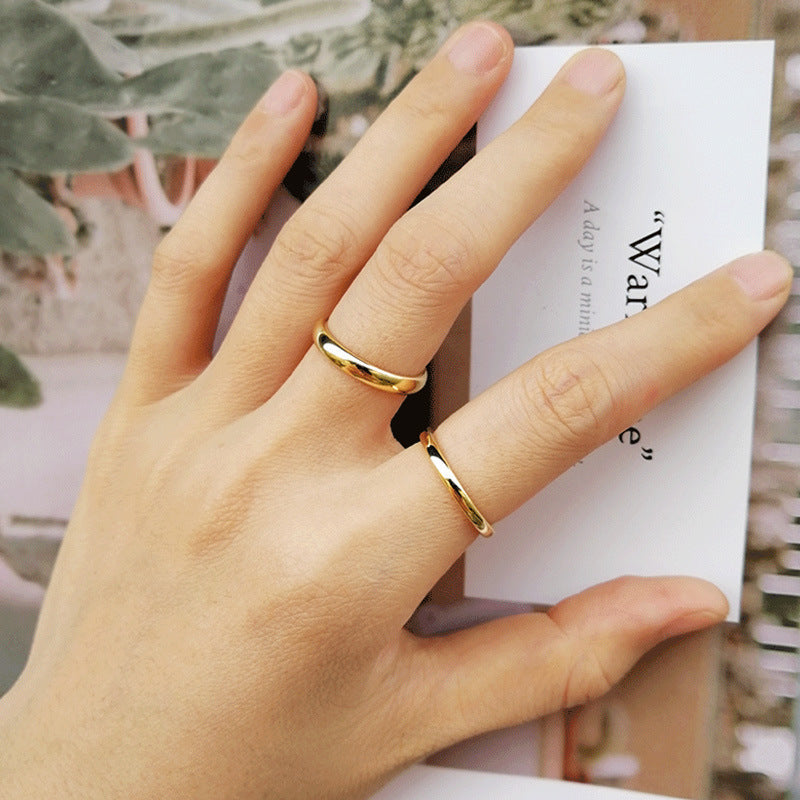 Hand wearing two gold rings on a blurred background