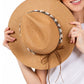 Woman holding a straw hat with decorative band against a white background