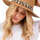 Woman wearing a tan straw hat with decorative band on a white background