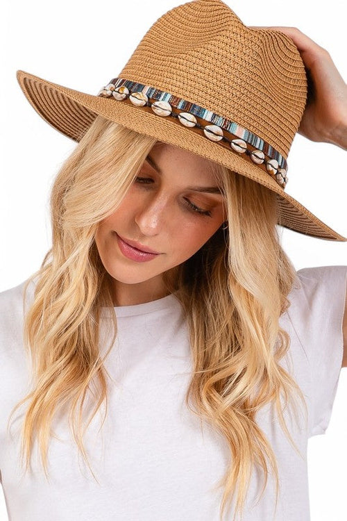 Woman wearing a tan straw hat with decorative band on a white background