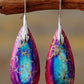 Teardrop-shaped earrings with purple and blue marbled design hanging on a branch.