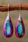 Teardrop-shaped earrings with purple and blue marbled design hanging on a branch.