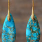 Turquoise teardrop earrings with gold hooks on a blurred background