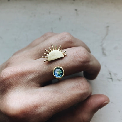Hand wearing two gold rings with unique designs on a neutral background