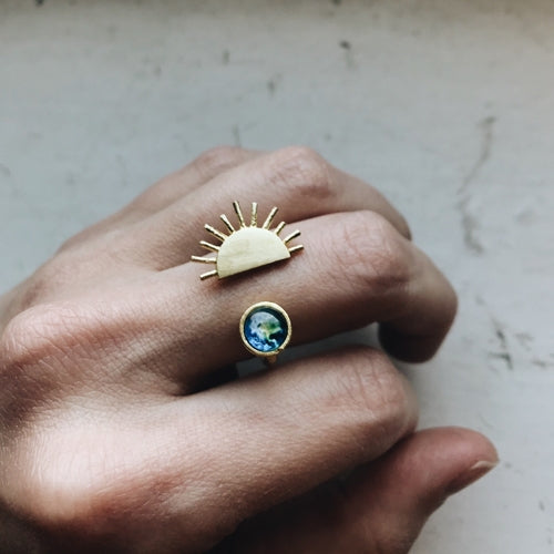Hand wearing two gold rings with unique designs on a neutral background