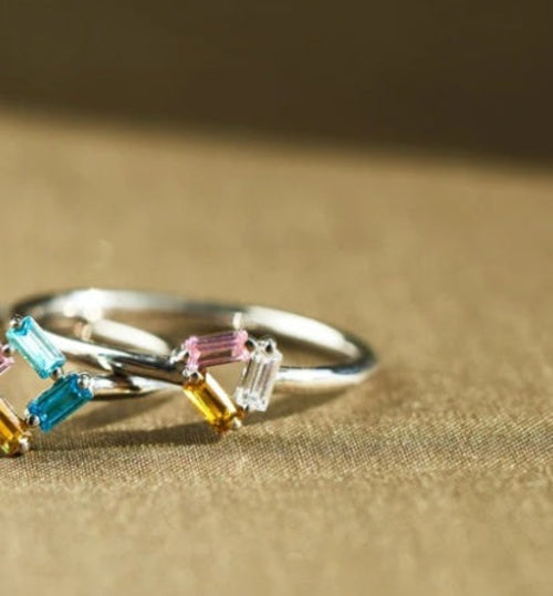 Silver ring with colorful gemstones on a beige fabric background